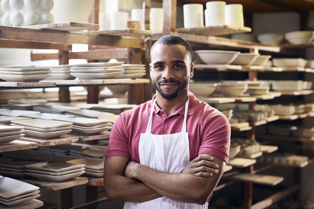 Man in apron crossing arms in pottery factory